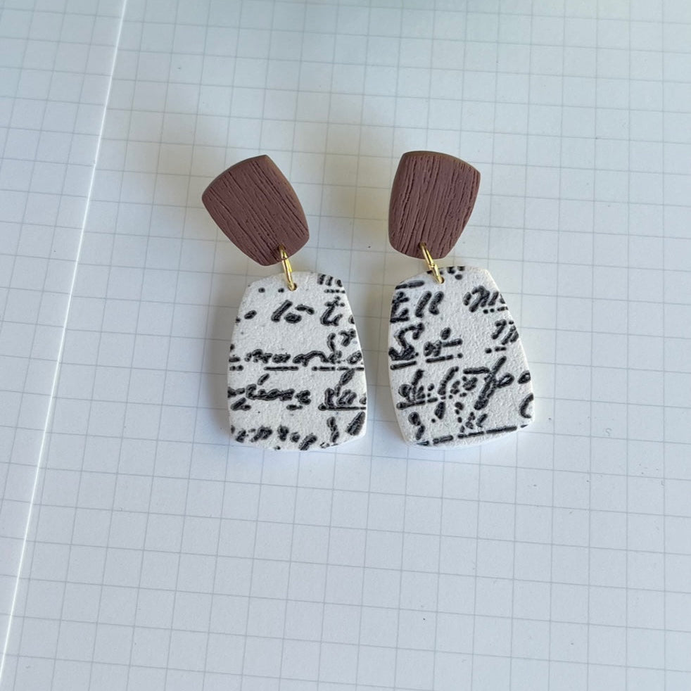 Pair of earrings with brown tops and black and white patterned bottoms on a grid background.