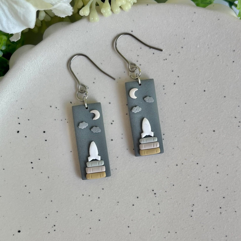 Earrings with rocket design on a speckled surface with flowers in the background