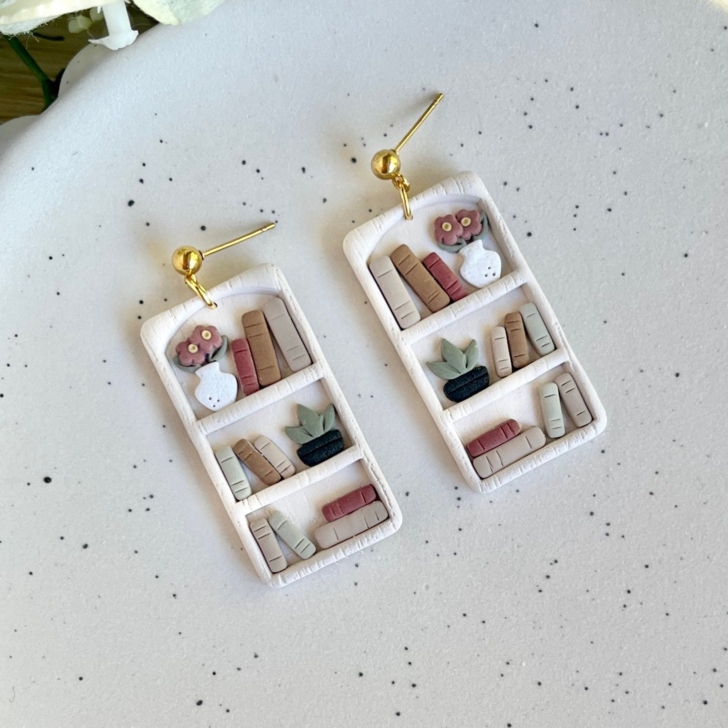 A pair of earrings designed to resemble bookshelves with books, crafted from gold-plated stainless steel.