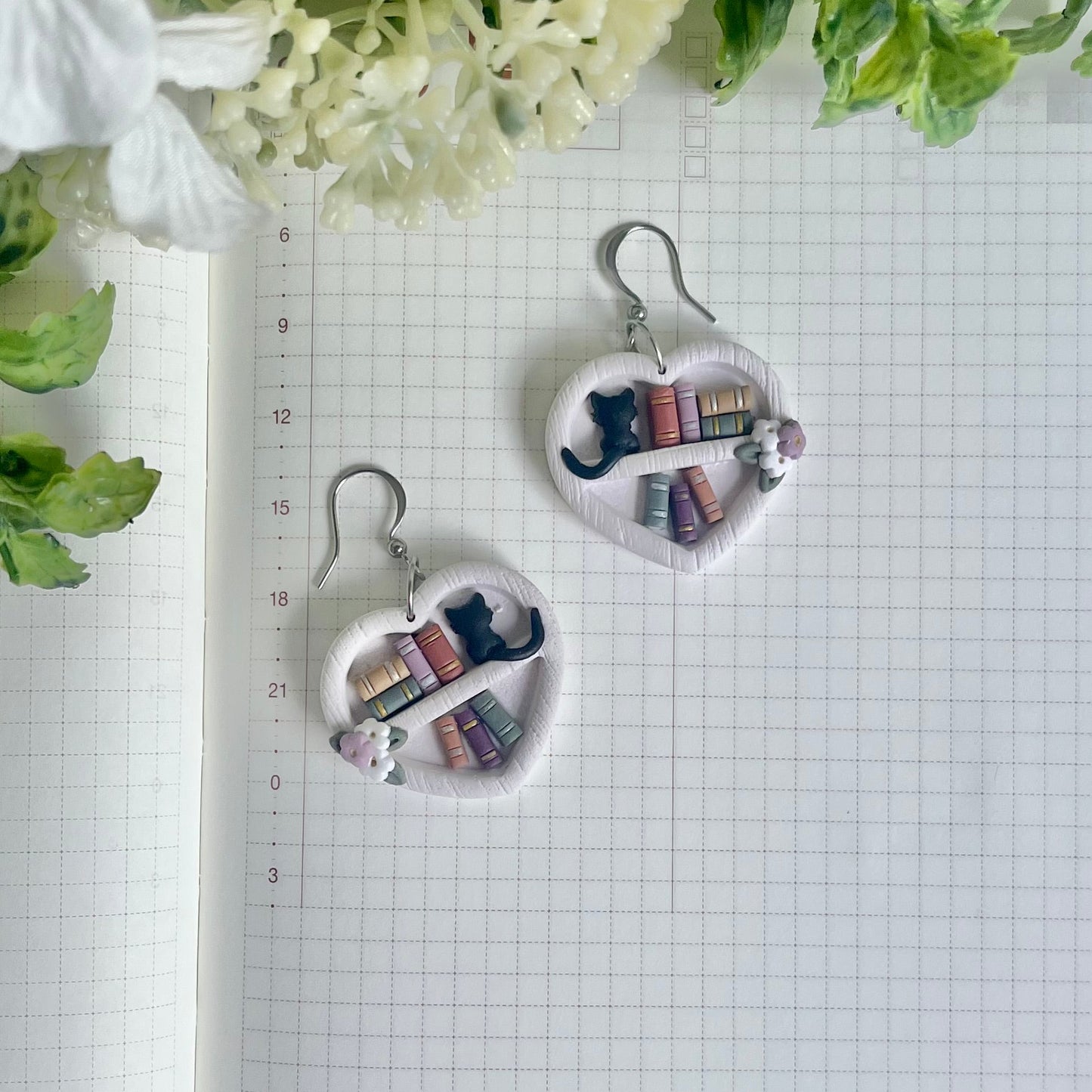 Heart-shaped earrings with book design on a grid background with flowers.