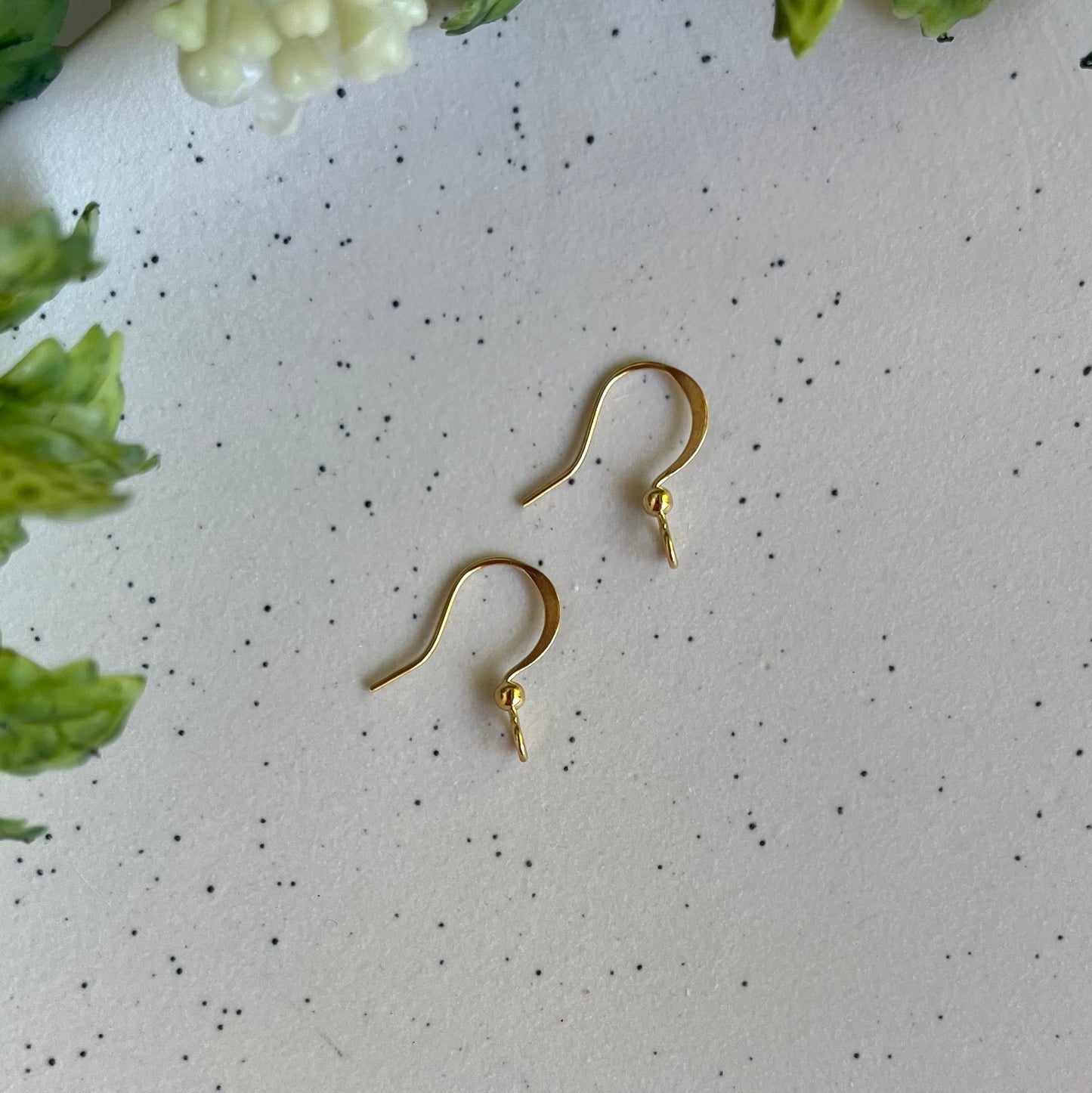 Gold earrings on a speckled white surface with green leaves and flowers.
