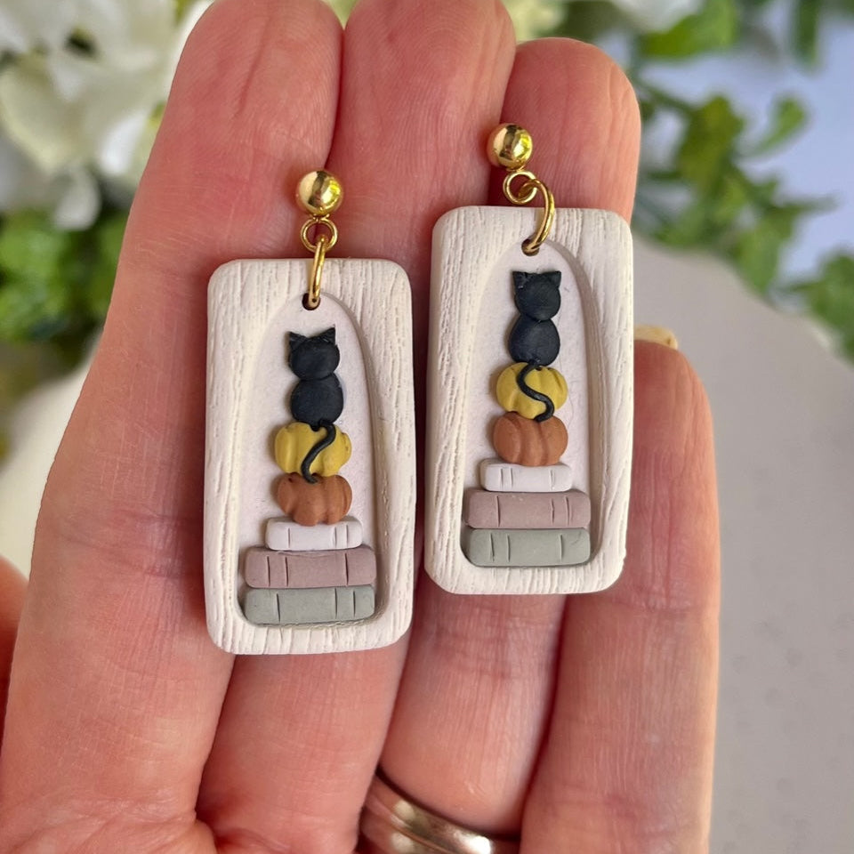 Pair of earrings with cat designs held in a hand against a blurred natural background