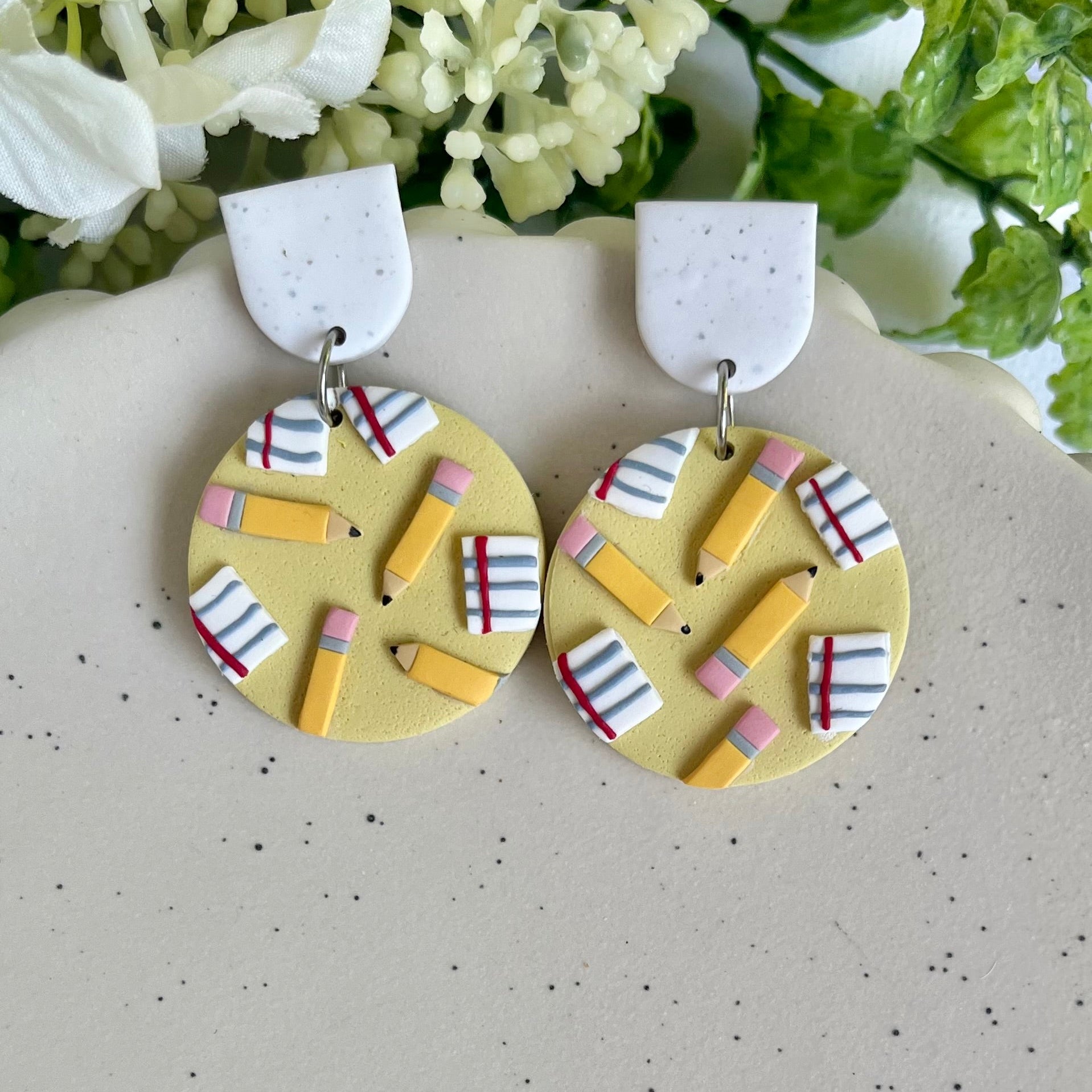 Pair of earrings with colorful geometric design on a speckled surface with flowers in the background