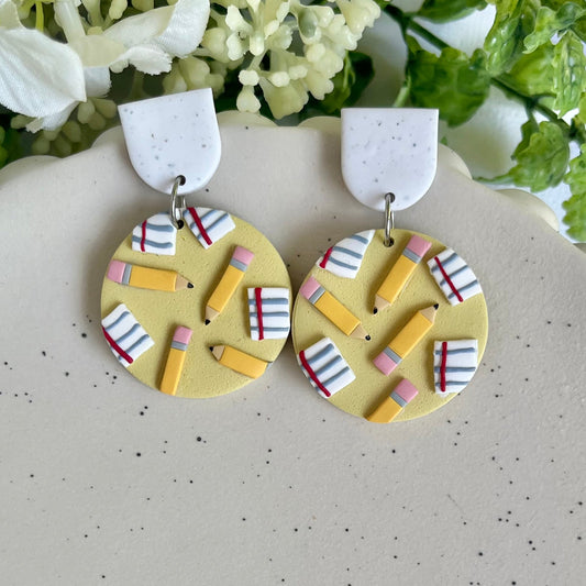 Pair of earrings with colorful geometric design on a speckled surface with flowers in the background