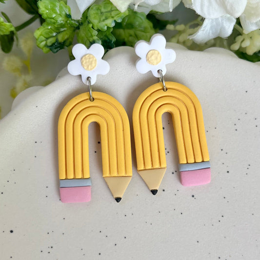 Pencil-shaped earrings with white flowers on a speckled surface.