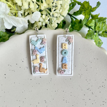 Pair of earrings with letter 'M' design on a speckled surface with flowers in the background