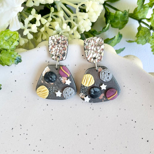 Pair of earrings with colorful designs on a white surface with greenery in the background