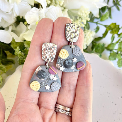 Hand holding a pair of earrings with a floral background