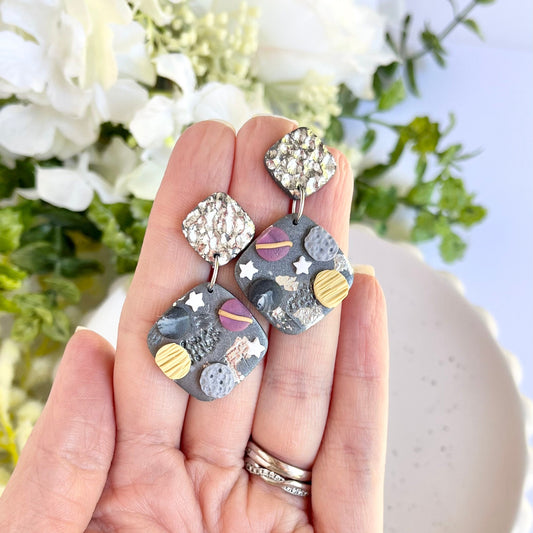 Hand holding a pair of earrings with a floral background
