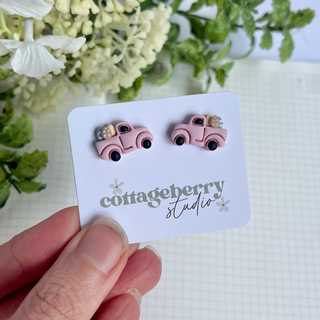 Pink car-shaped earrings on a Cottageberry Studio card with flowers in the background